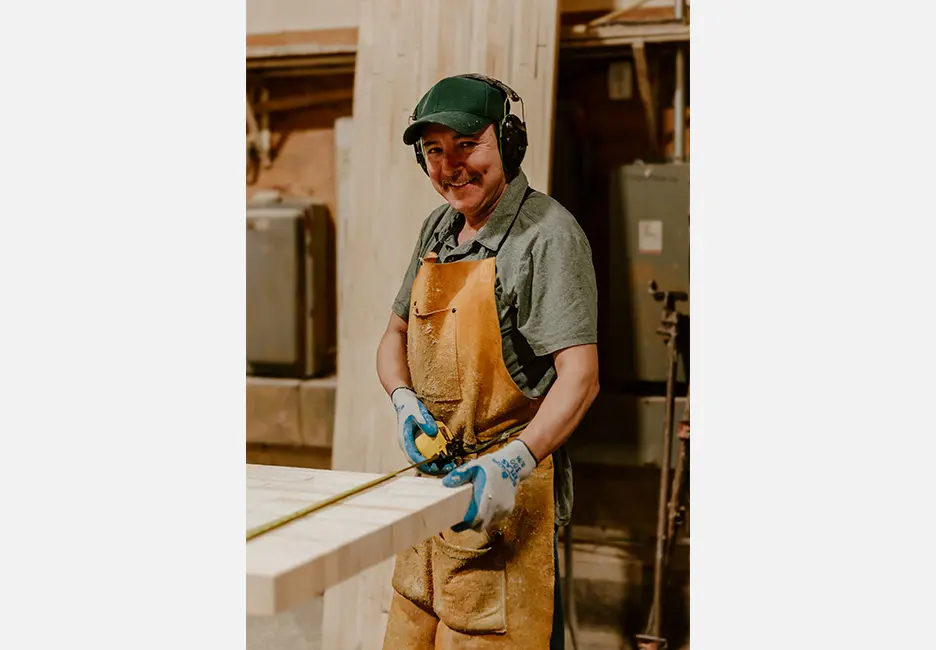 A man in an apron and hat is working on wood.